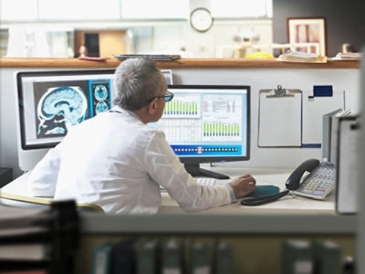 Medical professional viewing brain scans and data charts on a computer.