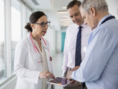 Doctor discussing medical scans with two colleagues on a tablet.