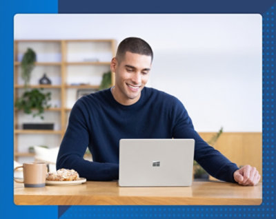 Person using a laptop at a desk with a cup and pastry nearby.