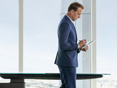 Professional using a tablet and stylus while standing in a modern office with floor-to-ceiling windows.