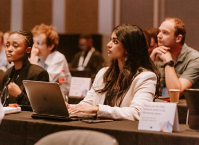 People seated at a conference table during a seminar, with laptops, notebooks, and name placards visible.