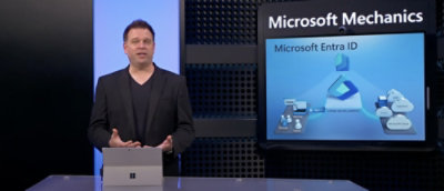 A man standing in front of a computer screen displaying the text Microsoft Mechanics and Microsoft Entra ID.