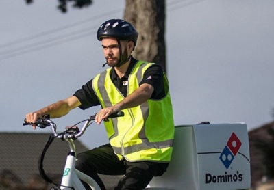 A person wearing a reflective vest and helmet riding a bicycle with Domino's text visible.