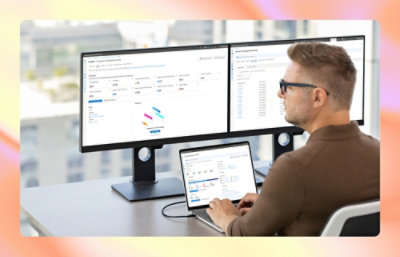 A person sitting at a desk with a laptop and multiple monitors.