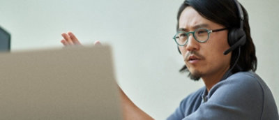 A person wearing headphones and glasses while looking at a computer screen.