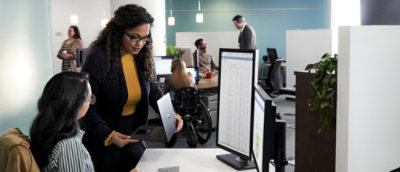 A woman wearing a yellow shirt and black jacket looks at a laptop.