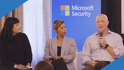 Một nhóm người đang ngồi trước màn hình màu xanh lam có biển hiệu Microsoft Security.