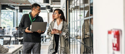 Un homme et une femme se tenant dans un bureau, l’homme tenant un ordinateur portable et la femme tenant un téléphone.