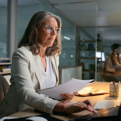Personne en costume blanc assis à un bureau avec un ordinateur portable et tenant un morceau de papier.