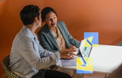 Two people collaborating at a table using a laptop with a digital interface overlay
