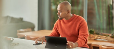 A person sitting at a table using a laptop and holding a phone.