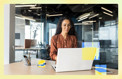 A person sitting at a desk using a laptop with a white rectangular object nearby.