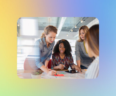 Four women collaborating over documents on a table in a brightly lit office.