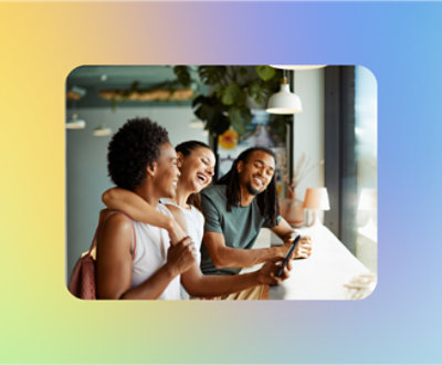 Three friends laughing and looking at a smartphone together in a modern café.