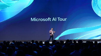 Presenter on stage at Microsoft AI Tour speaking to a large audience in an auditorium.