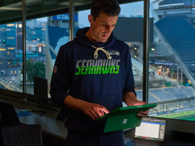 NFL Seattle Seahawks staff member using a Microsoft Surface Pro tablet in a stadium suite, with stadium seating in the background.