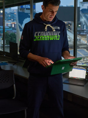 NFL Seattle Seahawks staff member using a Microsoft Surface Pro tablet in a stadium suite, with stadium seating in the background.