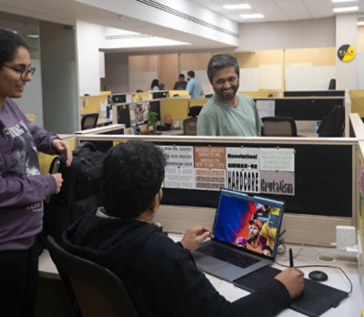 A group of people working in an office with laptops and other equipment visible.