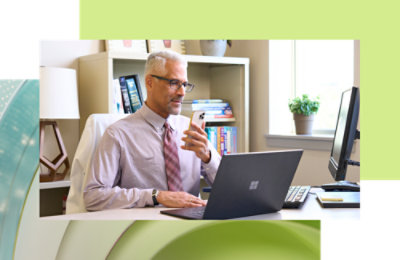 Muškarac sedi za radnim stolom na kojem se nalaze laptop i telefon.