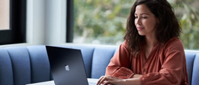 Žena sa dugom smeđom kosom sedi za stolom i koristi laptop.