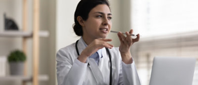 Doktor u belom mantilu, sa stetoskopom, govori u pametni telefon dok gestikulira drugom rukom.