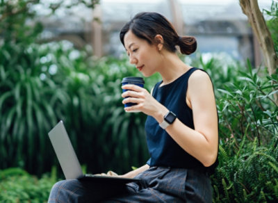 A person sitting on a bench with a laptop and a cup of coffee.