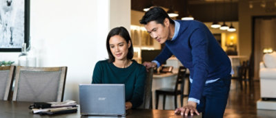 A man standing behind a woman who is using a laptop.