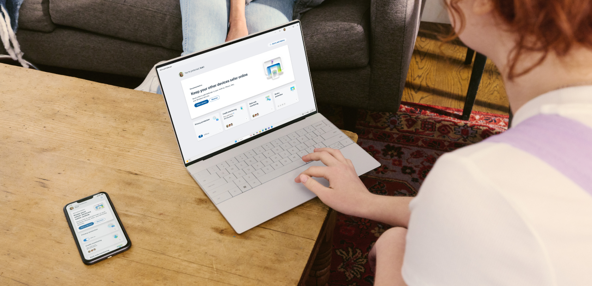 Person sitting at a table with a laptop and cell phone with Microsoft Defender on screen