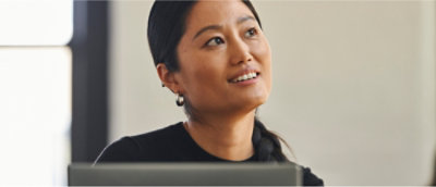 Persoon met lang donker haar en oorbellen die in een goed verlicht interieur omhoog kijkt en glimlacht.