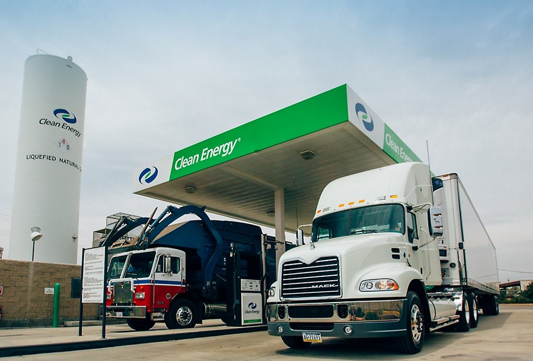 Trucks refueling at a clean energy station offering liquefied natural gas, under a clear sky.