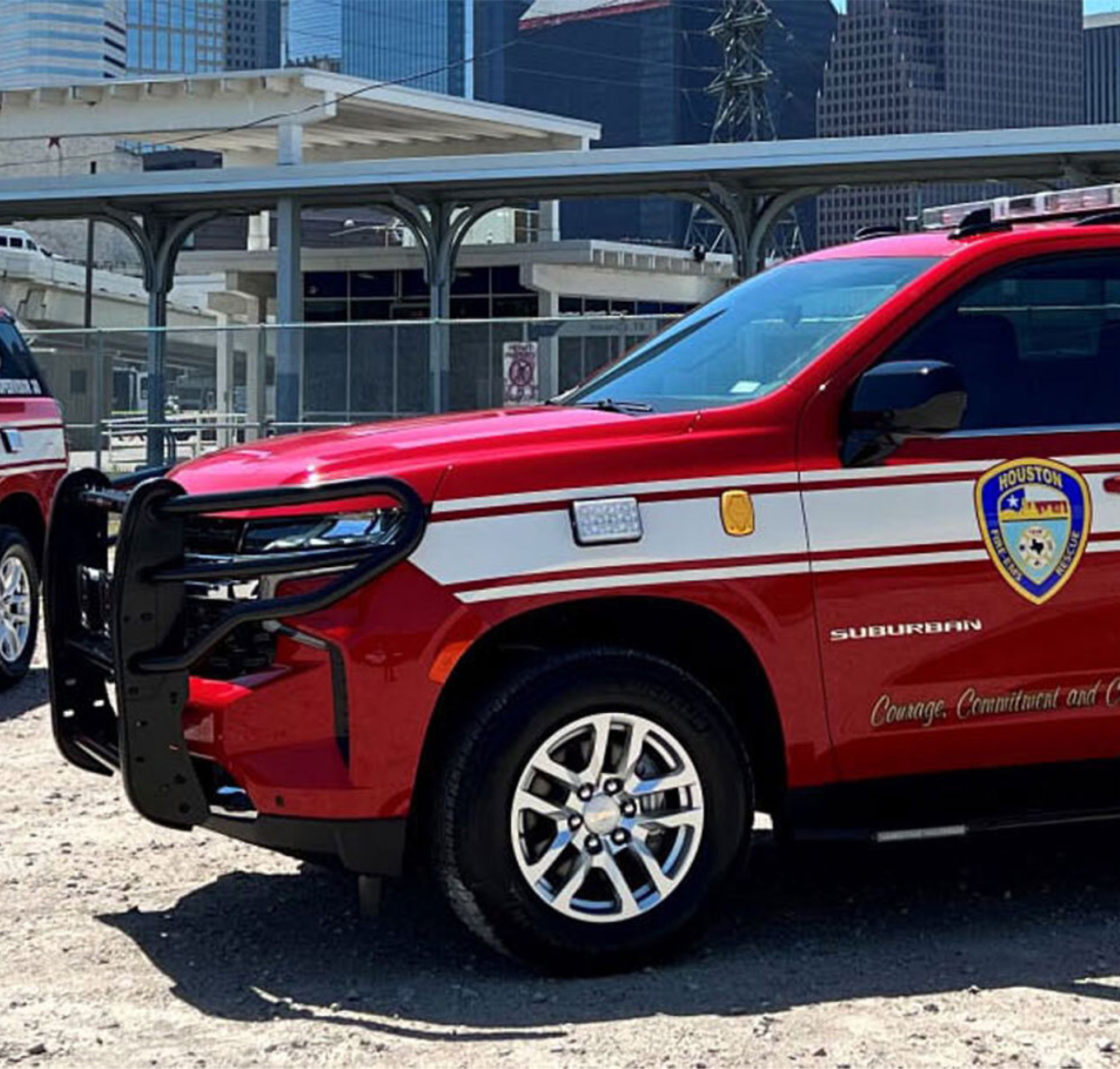 Czerwona furgonetka Staży Pożarnej miasta Houston zaparkowana na zewnątrz z budynkami miejskimi w tle.