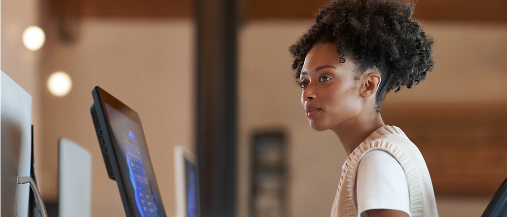Een jonge zwarte vrouw die gelijktijdig op een computer in een moderne kantooromgeving werkt.