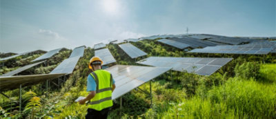 A man in a yellow vest standing in front of solar panels.