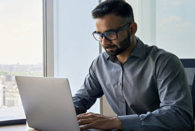 A man in a gray shirt and glasses working on a computer