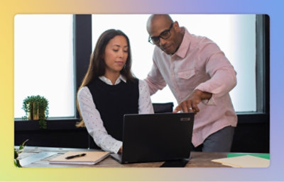 ノート PC の画面を見ながら女性と話し合っている眼鏡をかけた男性