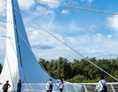 Mehrere Personen gehen über eine Brücke unter blauem Himmel mit Wolken und einer sichtbaren Stromleitung.