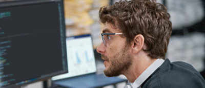 Ein Mann mit lockigen Haaren, der Brille trägt und auf einen Computerbildschirm schaut