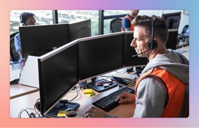 Ein Mann, der ein Headset trägt und an einem Schreibtisch mit mehreren Computerbildschirmen sitzt.