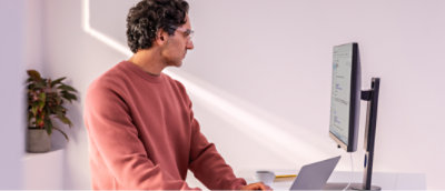 A man in a red sweater sitting at a desk using a laptop.