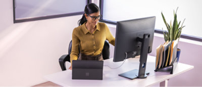 一位穿黄色衬衫的女士坐在桌旁，上面放着一台计算机。