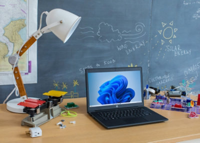 Письменный стол с ноутбуком и лампой на фоне школьной доски с набросками идей из области возобновляемой энергии.