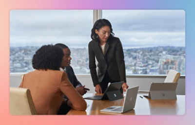 Three people in a meeting room with laptops, engaged in discussion.