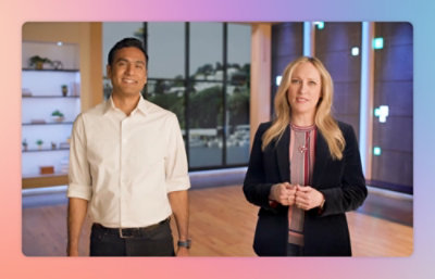 A man and woman stand side by side in a modern indoor setting, both looking at the camera.