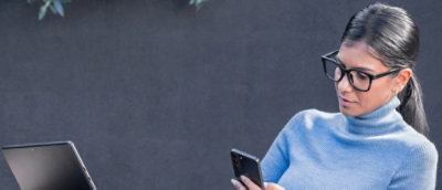 A woman wearing glasses and a blue turtleneck, holding a phone.