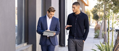 Two men walking and conversing in a modern office hallway.