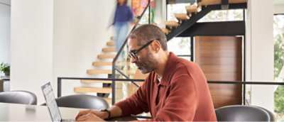 Человек в очках работает на ноутбуке за столом.