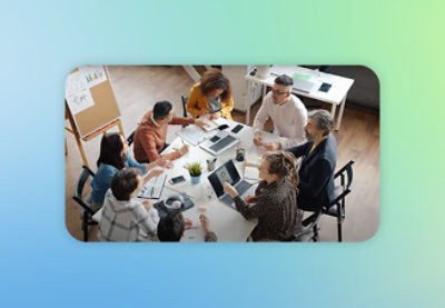 Группа из восьми человек сидит за столом и сотрудничает в офисе. На столе стоят ноутбуки.