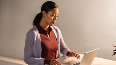 Person standing indoors holding a laptop in front of a bookshelf and a sofa.