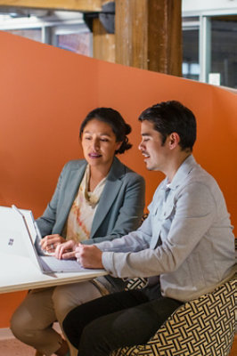A man and woman sitting at a table looking at a laptop.