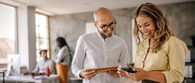 A woman and man joyfully view a smartphone together in a sunlit office.
